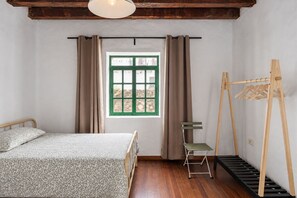 Een slaapkamer met een bed, een raam met gordijnen, een stoel en een houten kapstok.