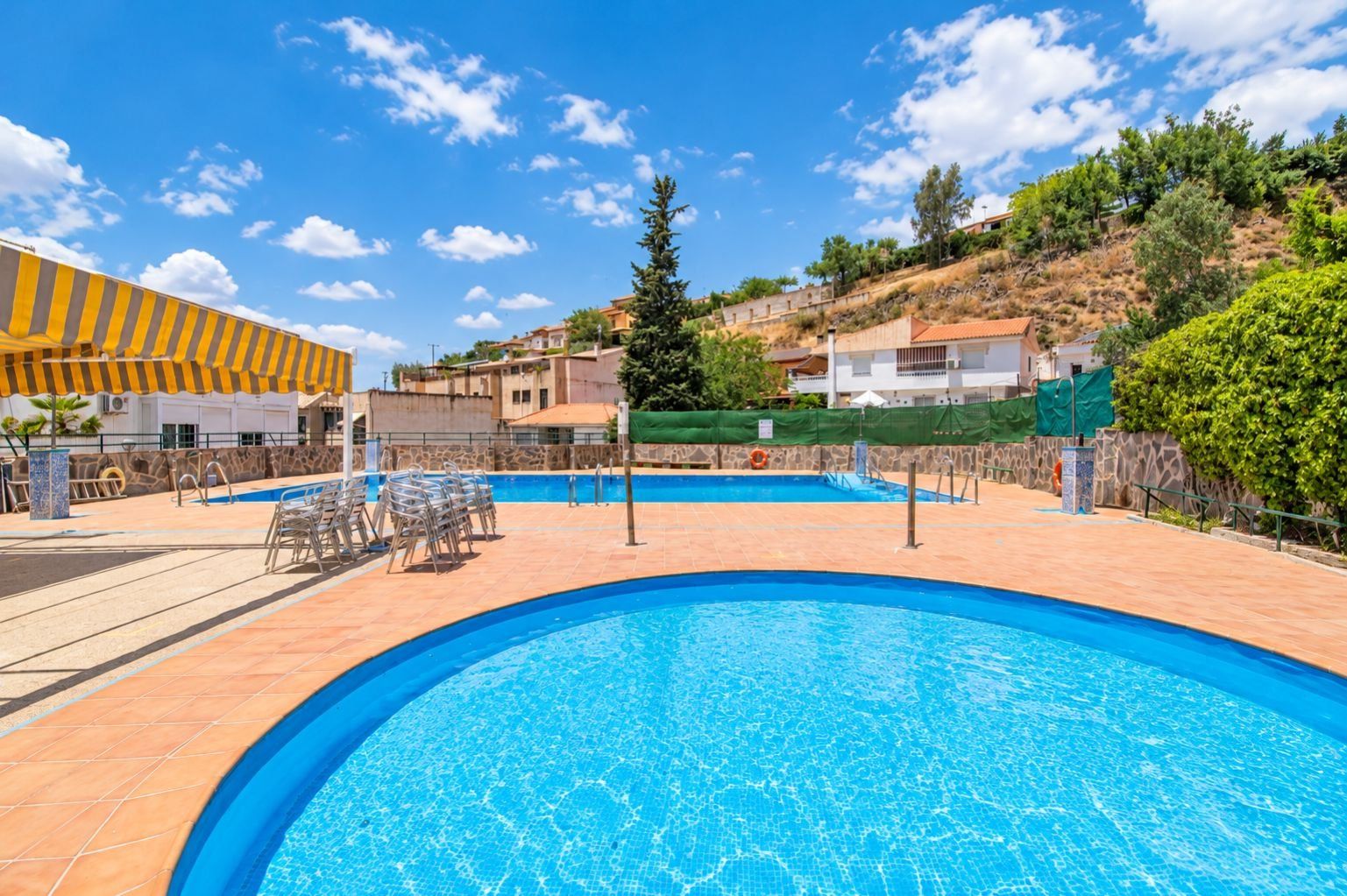 A swimming pool with tiled deck, lounge chairs, and a covered seating area.