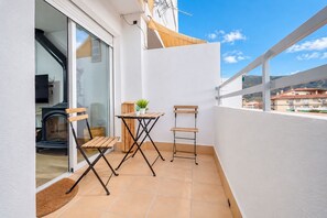 Ein Balkon mit einer Holzbank, einem kleinen Tisch mit Blumentöpfen und Blick auf die umliegenden Gebäude.