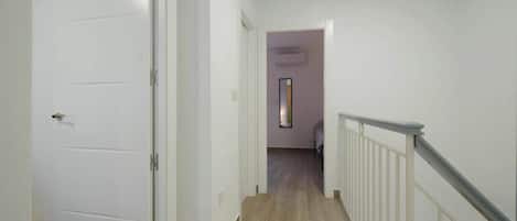 Un pasillo con suelo de madera, paredes blancas y una puerta blanca a la izquierda.