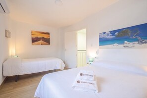 Ett hotellrum med två sängar, en tavla som föreställer en solnedgång, en tavla som föreställer en strand och en handduk med logotypen ”guestready”.