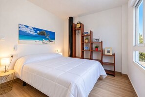 Ein Hotelzimmer mit einem Bett, einer Wanduhr, einem Regal mit Dekoration und einem Gemälde, das eine Strandansicht zeigt.