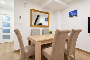 En matplats med ett träbord, beige stoppade stolar, en spegel, en krukväxt och en inramad tavla på väggen.