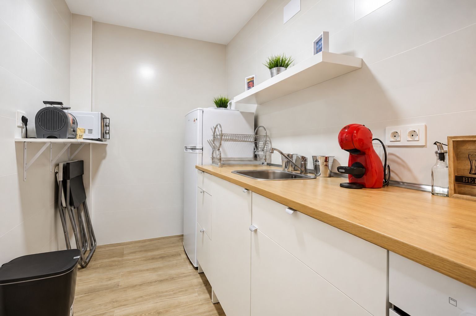 Una cocina compacta con un lavamanos, una cafetera roja y un refrigerador blanco.