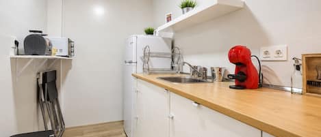 Una cocina compacta con un lavamanos, una cafetera roja y un refrigerador blanco.
