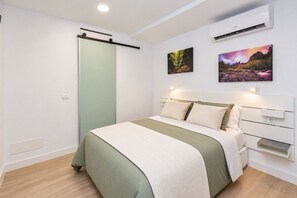 Un dormitorio con cama, una puerta corredera, un aire acondicionado de pared y dos cuadros de paisajes.