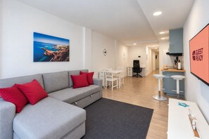 A modern living room with a grey sofa, red cushions, a dining area with white chairs, and a kitchen area with a bar counter. - GuestReady - Beach Escape by Cancajos (Breña Baja)