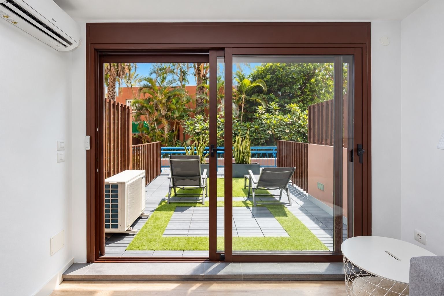 A modern room with a sliding glass door leading to an outdoor patio with a pool, chairs, and a small table.