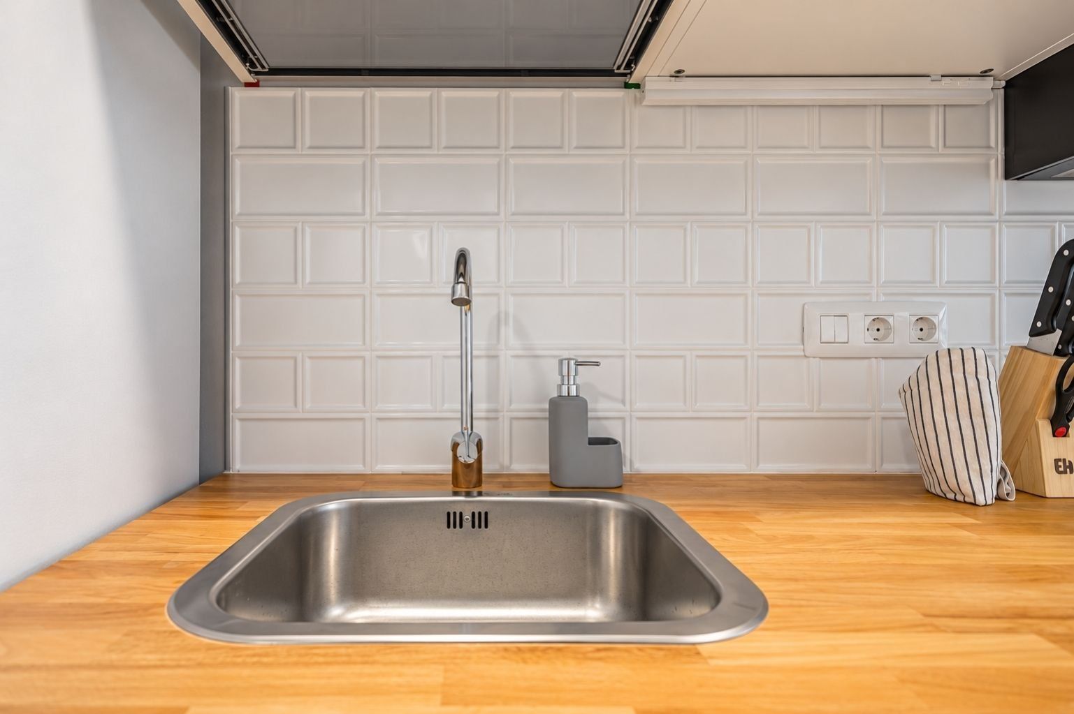 Eine moderne Küche mit Spüle aus Edelstahl, einem Wasserhahn, einer Seifenspender und einer gestreiften Tasche auf der Arbeitsplatte.