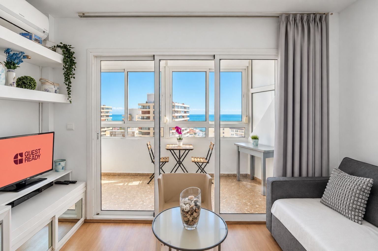 A modern hotel room with a balcony, a sofa, a TV, and a dining area.
