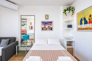 A modern hotel room with a bed, a sofa, a glass table, and a painting on the wall. - GuestReady - Las Dalias Torremolinos Comfort (Torremolinos)