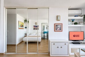 A modern hotel room with a sliding door leading to a bedroom, a desk with a computer, and a TV displaying 'GUEST READY'. - GuestReady - Las Dalias Torremolinos Comfort (Torremolinos)