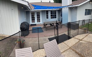 Ein überdachter Patio-Bereich mit Tisch, Stühlen, einem Grill und einem Blumentopf.