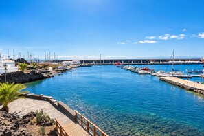 A marina with boats docked, a clear blue sky, and a rocky shoreline with vegetation. - GuestReady - Beachfront Apartment Marina Views (La Restinga)