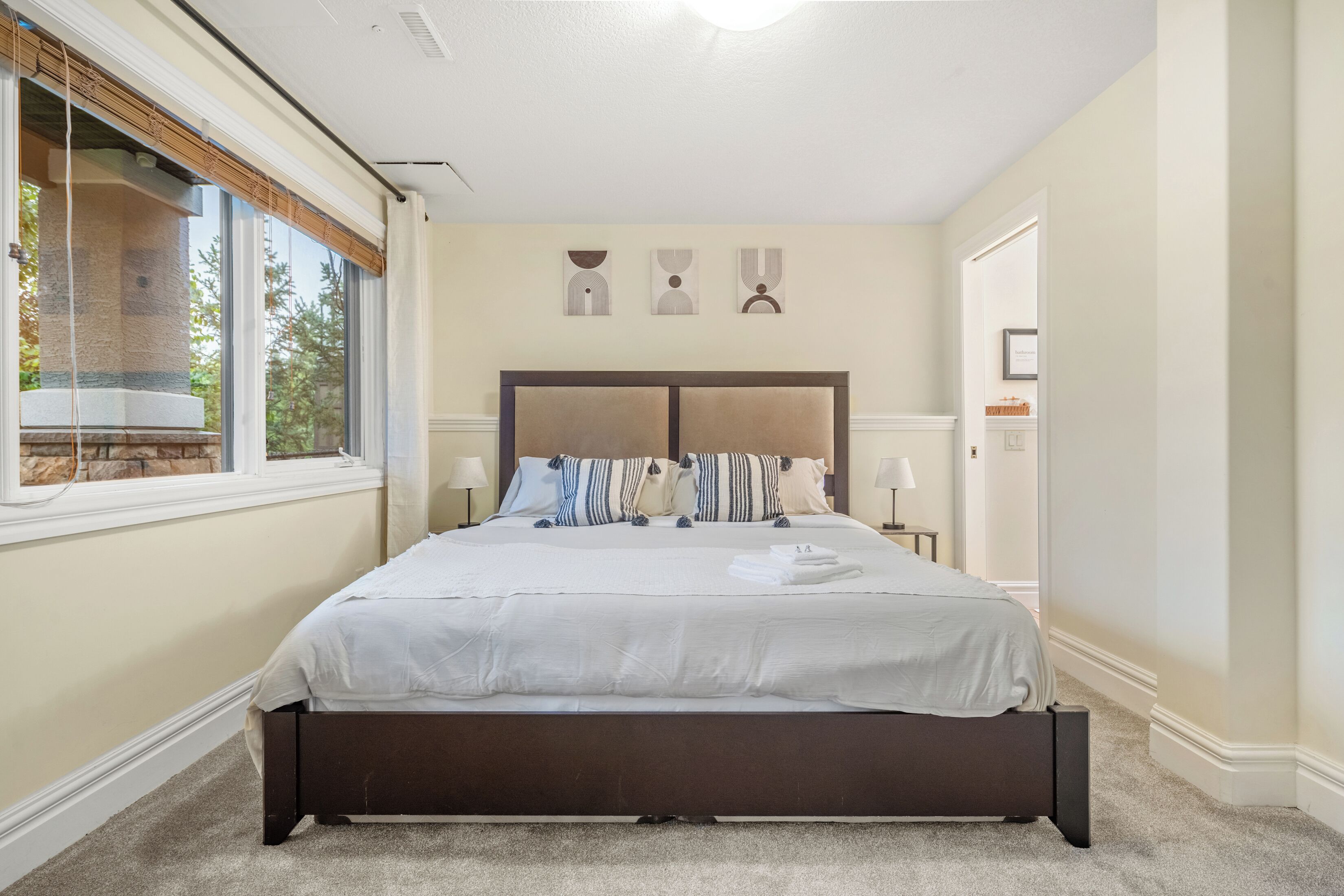 Ein Schlafzimmer mit einem großen Bett, einem Fenster mit Jalousien, einer Steinsäule und Blick ins Freie.