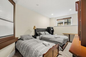 A bedroom with two beds, a nightstand, a lamp, and a window. - 4BR Walkout Suite | Private Sauna, Backyard & Fish Creek Trails (Calgary)