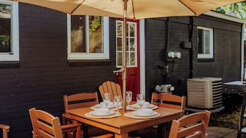 Une terrasse extérieure avec une table en bois dressée pour le repas, entourée de chaises, et protégée par un grand parasol.