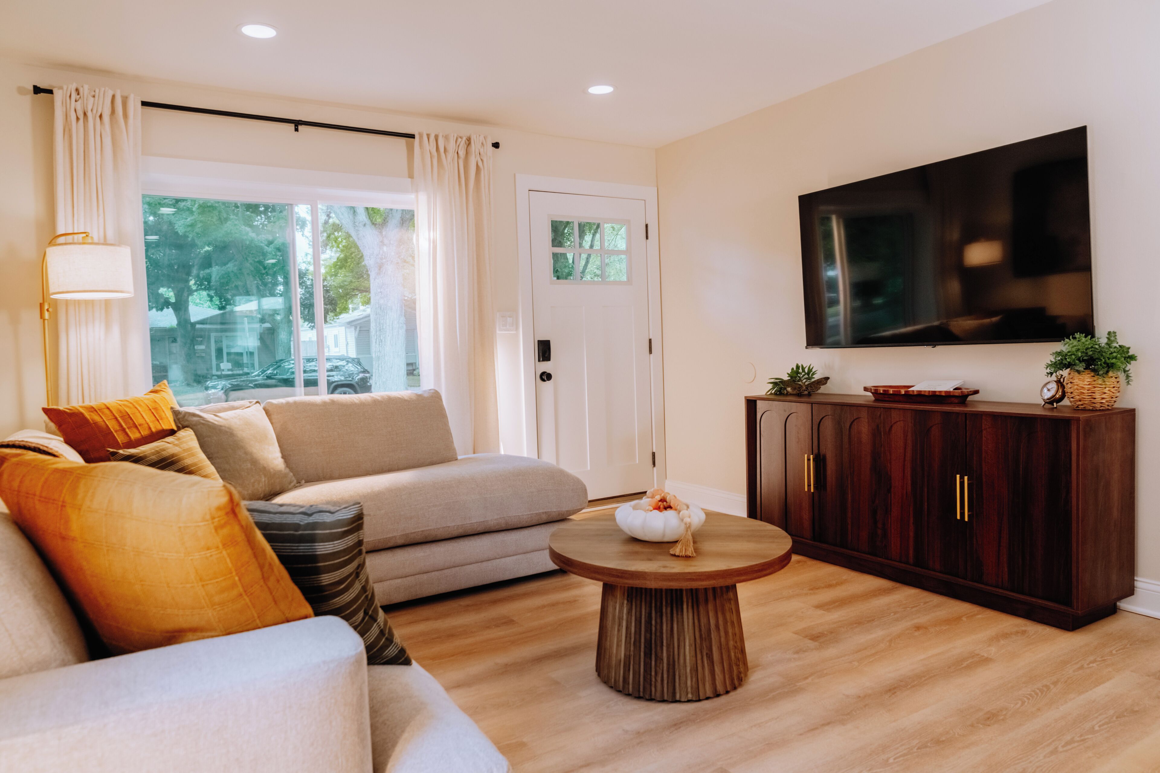 Una sala de estar con un sofá, una mesa de centro, un aparador, un televisor y una puerta.