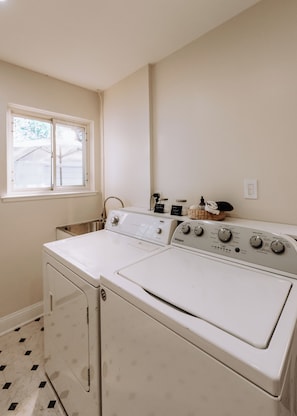 Een wasserette met twee gestapelde wasmachines en drogers, een raam en een wandmand.
