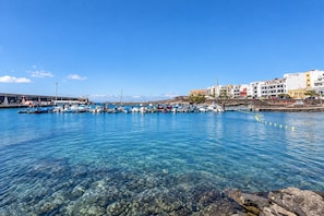 Marina com barcos atracados, água cristalina e edifícios ao fundo.