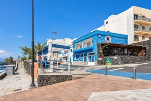 Un carrer marítim amb un edifici blau anomenat 'EL RINCÓN' i un restaurant de façana de pedra.