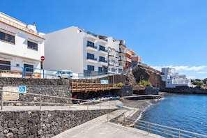Um edifício costeiro com parede de pedra, rampa acessível para cadeiras de rodas e céu azul límpido.