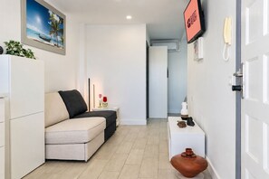 Quarto de hotel com sofá, mesa de cabeceira com um vaso, telefone e um quadro na parede.