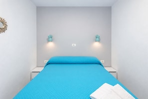 Un llit individual amb un estovat blau en una habitació amb parets grisclates.