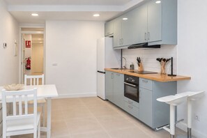 Une cuisine moderne avec des meubles bleu clair, un plan de travail en bois et un coin repas blanc comprenant une table et des chaises.