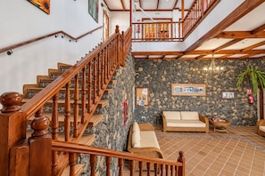 A wooden staircase leading to a living area with a stone wall, a sofa, and a wicker chair. - GuestReady - Garden Retreat with Pool (Santa Cruz de Tenerife)