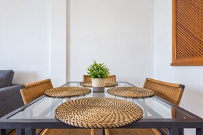 Una mesa de comedor con cubierta de vidrio, rodeada de sillas tejidas, una planta en maceta y un mantel individual tejido.