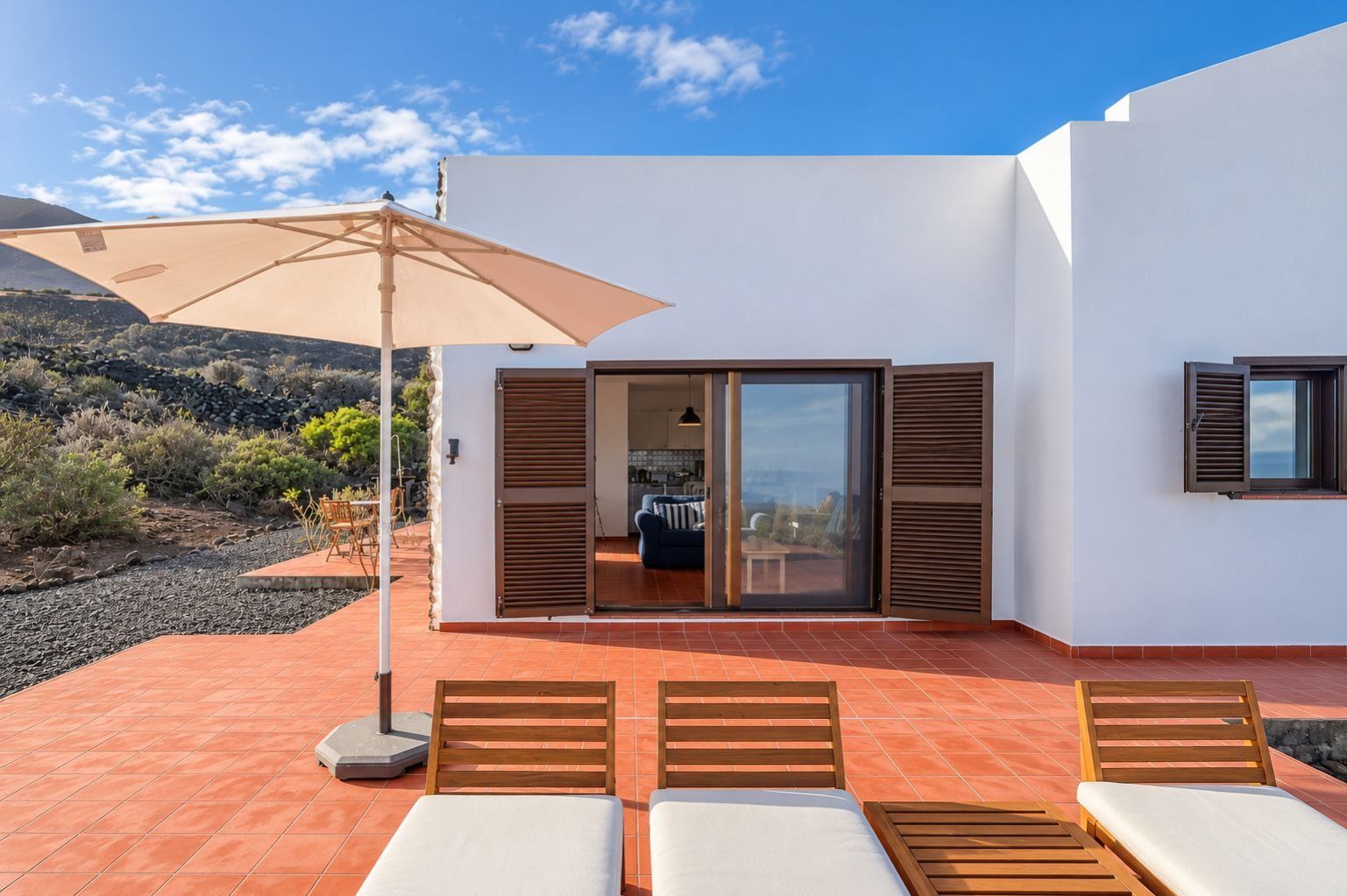 Un patio moderno al aire libre con una zona de estar, una puerta corrediza de vidrio que da a un espacio interior y vistas del paisaje circundante.
