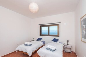 Une chambre avec deux lits, une fenêtre donnant sur un beau paysage, une table de chevet avec une lampe et un luminaire suspendu au plafond.