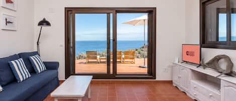 Un salón con un sofá, una mesa de centro y vista al mar por un ventanal corredero.