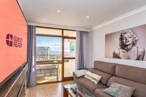 Ein Hotelzimmer mit großem Fenster, einer Couch, einem Couchtisch und einem Gemälde an der Wand.