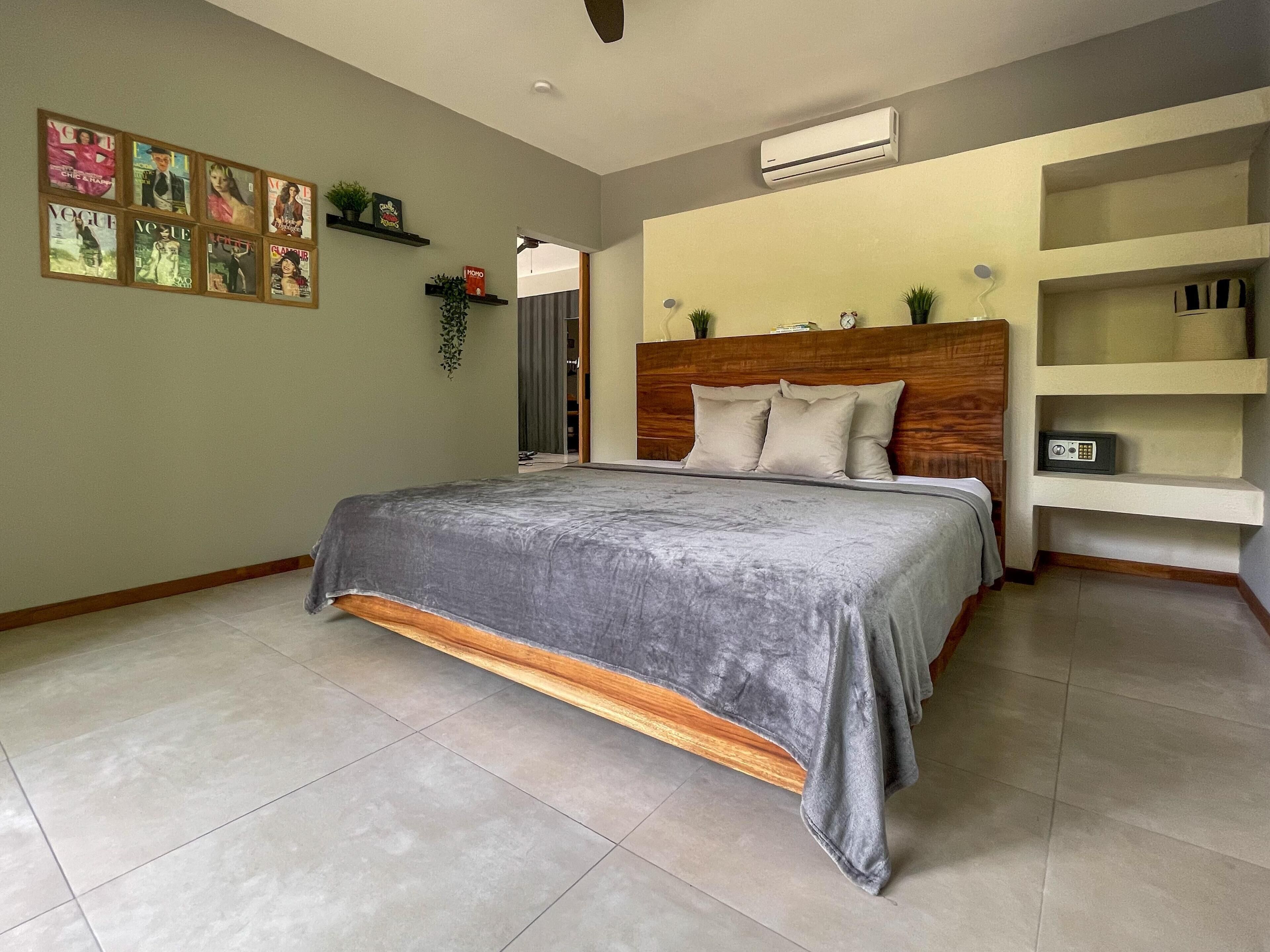 Un dormitorio con una cama, cabecera, estante con libros y aire acondicionado instalado en la pared.