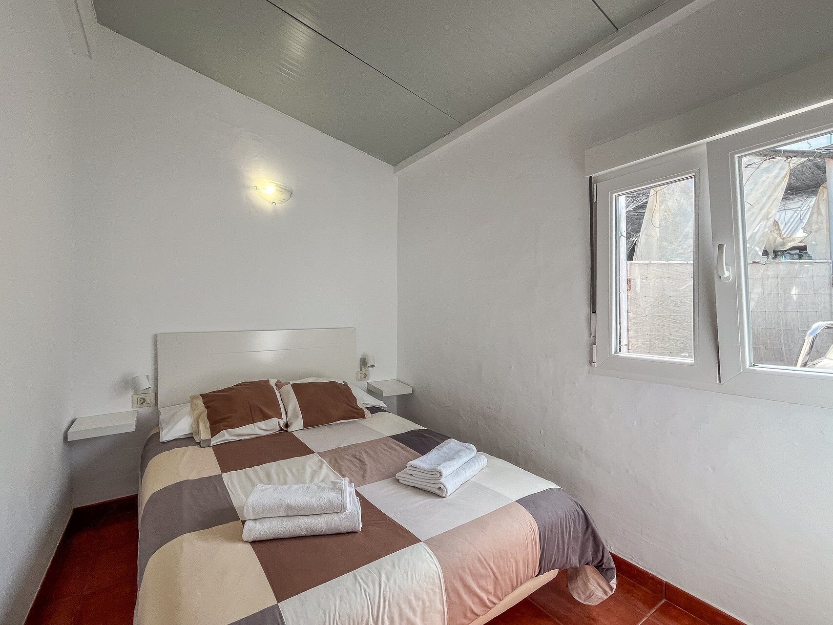 Un lit simple avec une tête de lit, une table de chevet avec une lampe et une fenêtre avec des rideaux.