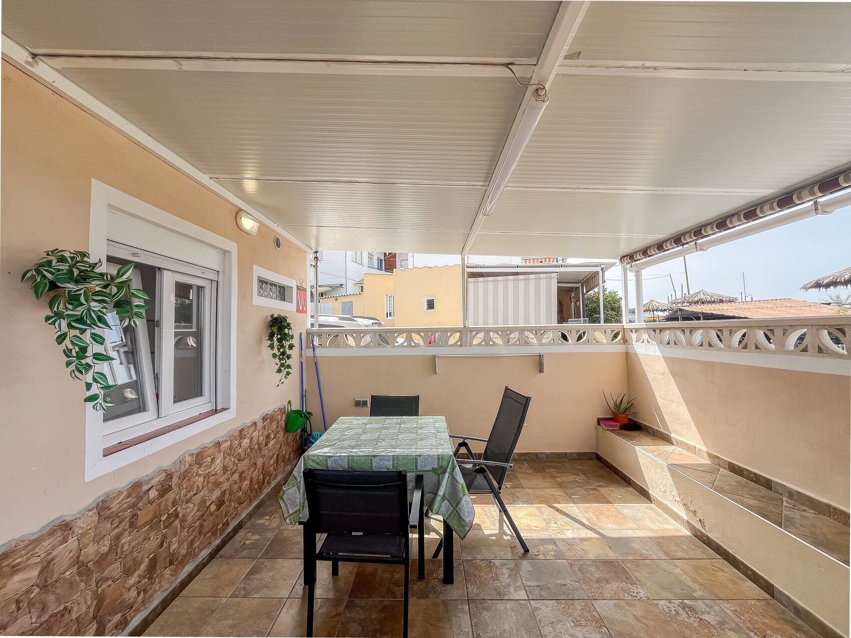 Une terrasse extérieure avec une table et des chaises, une fenêtre avec des stores et un mur décoratif.