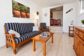 Ein Wohnzimmer mit einem gestreiften Sofa, zwei Sesseln, einem Holztisch und einer im Hintergrund sichtbaren Küche.