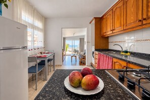 Eine Küche mit Essbereich und Blick ins Freie, auf der Arbeitsfläche ein Teller mit Obst.