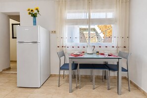 Eine Küche mit einem weißen Kühlschrank, einem Esstisch mit vier Stühlen und einem Fenster mit Vorhängen.
