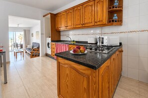 Une cuisine avec des meubles en bois, un plan de travail en granit, une cuisinière et un coin repas comprenant un canapé et des chaises.