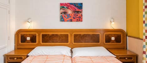 Ein Hotelzimmer mit einem hölzernen Kopfteil, zwei Nachttischen, einem Bett mit gestreifter Bettwäsche, einem Wandbild und einer Lampe auf jeder Seite des Bettes.