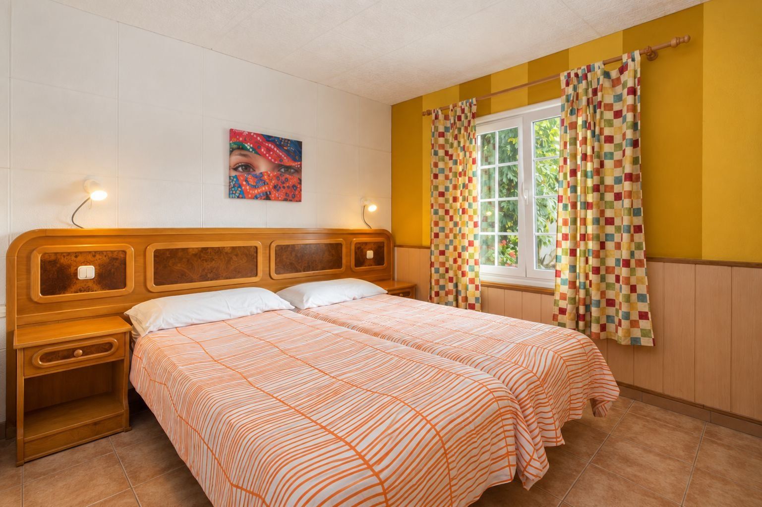 Ein Doppelbett mit gestreiftem Bettbezug, ein Nachttisch, eine Nachttischlampe, ein Fenster mit Vorhängen und ein Wandbild.