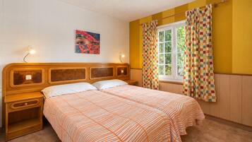 Ein Doppelbett mit gestreiftem Bettbezug, ein Nachttisch, eine Nachttischlampe, ein Fenster mit Vorhängen und ein Wandbild.