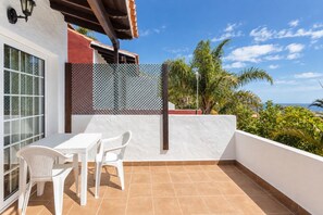 Varanda com mesa e cadeiras brancas, vista para o oceano e um cercado treliçado.