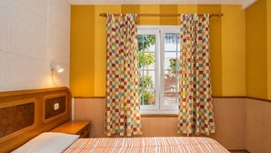 Un dormitori amb un llit, un ambossador de fusta, una finestra amb cortines i vista a l'exterior.