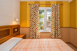 Quarto com cama, cabeceira de madeira, janela com cortinas e vista para o exterior.
