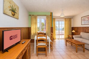 Habitación de hotel con comedor, televisor, sofá y vista al mar.