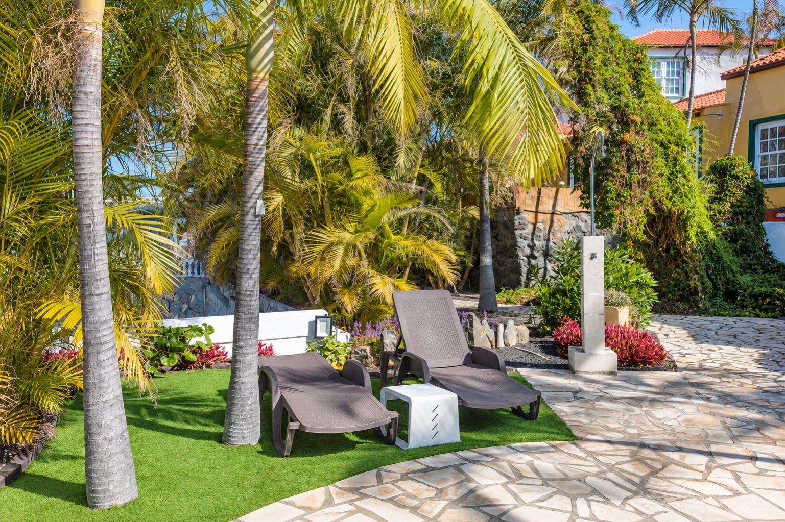 Un patio con dos sillones, una mesita y piso de baldosas de piedra.
